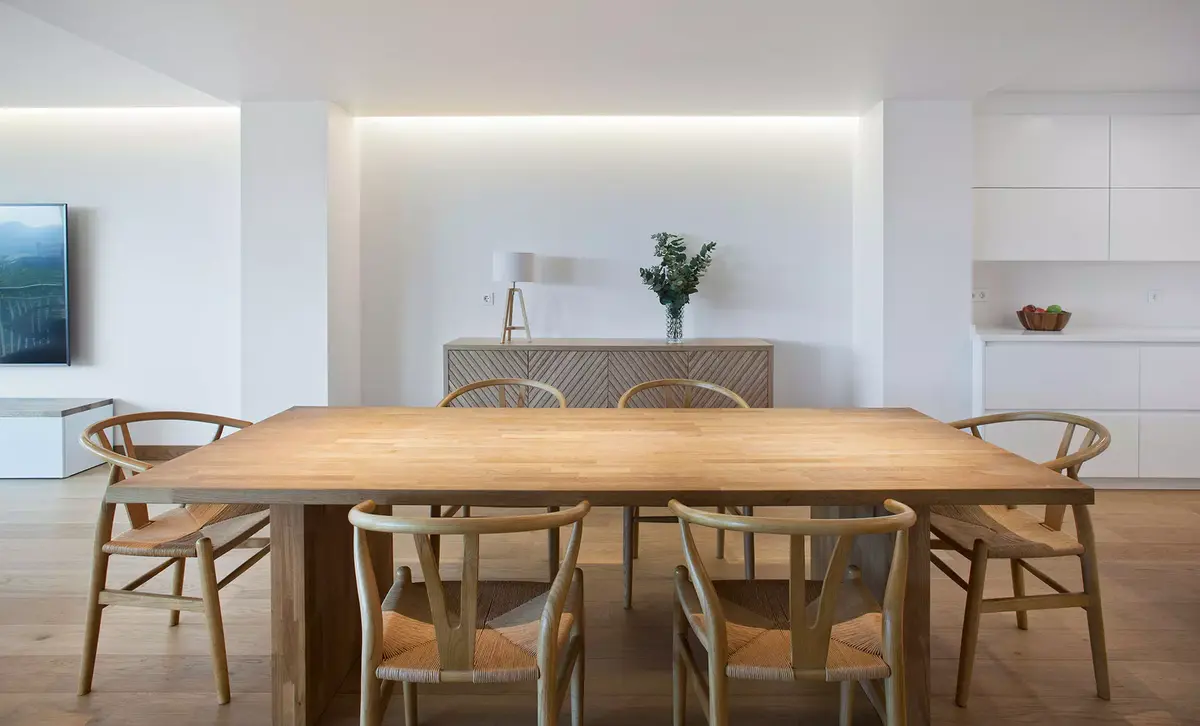 Comedor con mesa de madera y sillas de ratán en Ferrol. Rehabilitación de vivienda por SEA Arquitectos.