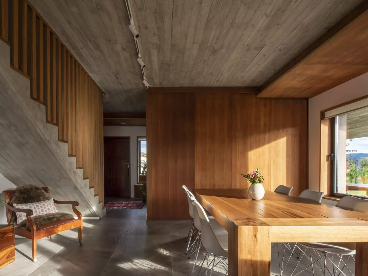 Comedor en vivienda en Narón con mesa maciza de madera, panelado de cedro y control de luz natural, espacio versátil con integración entre cocina y salón por SEA Arquitectos.